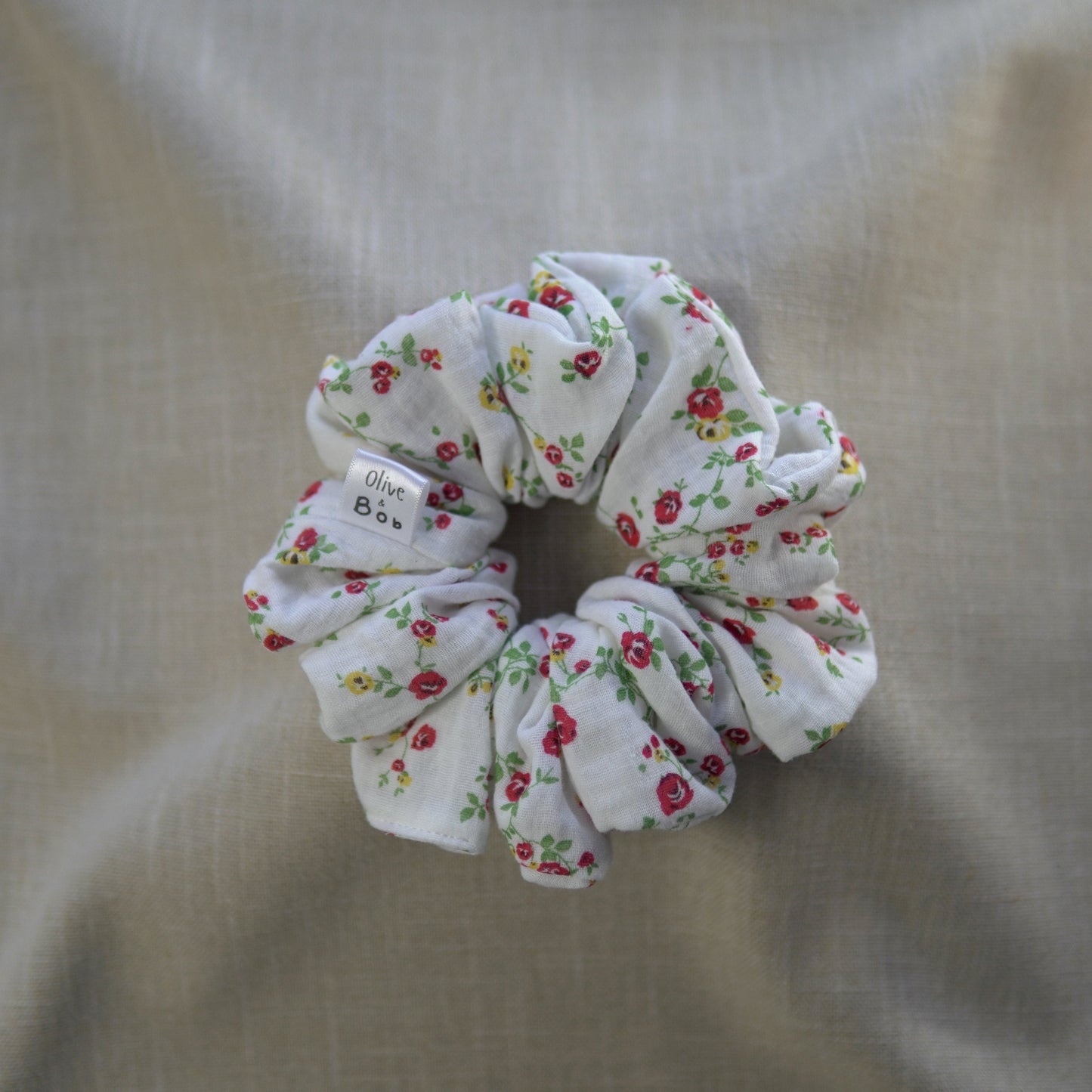 A handmade cheesecloth scrunchie with a white background, featuring a delicate floral pattern of red and yellow roses, designed for a lightweight and romantic touch