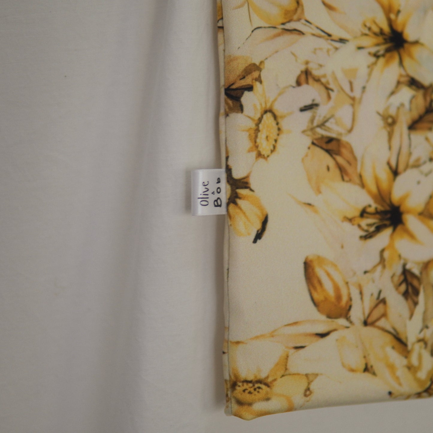 Close-up view of the yellow floral fabric tube top, focusing on the fabric tag that reads 'Olive Bob.' The tag is stitched into the left seam, with the background featuring the detailed golden-yellow flower pattern
