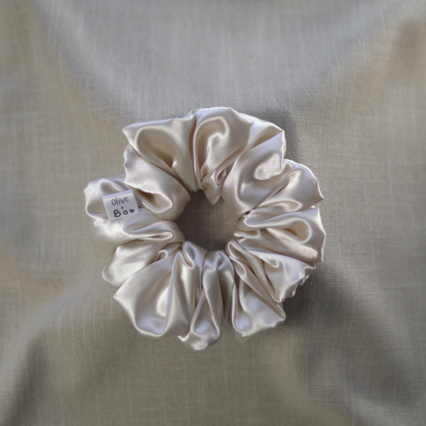A cream-colored satin scrunchie with a luxurious, smooth texture, designed to add elegance and shine to any hairstyle.