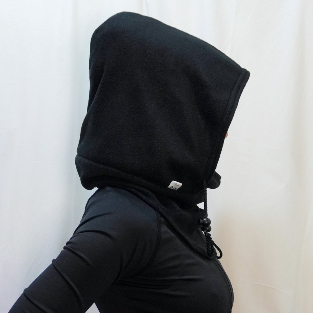 A handmade Noir Hoodeanie in solid black, displayed to show its soft, cozy fabric and new adjustable face panel feature. The design allows the hood to be pulled up snugly over the nose for added warmth and comfort, blending functionality with minimalist streetwear style.