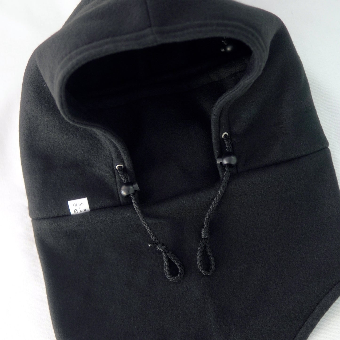 A handmade Noir Hoodeanie in solid black, displayed to show its soft, cozy fabric and new adjustable face panel feature. The design allows the hood to be pulled up snugly over the nose for added warmth and comfort, blending functionality with minimalist streetwear style.