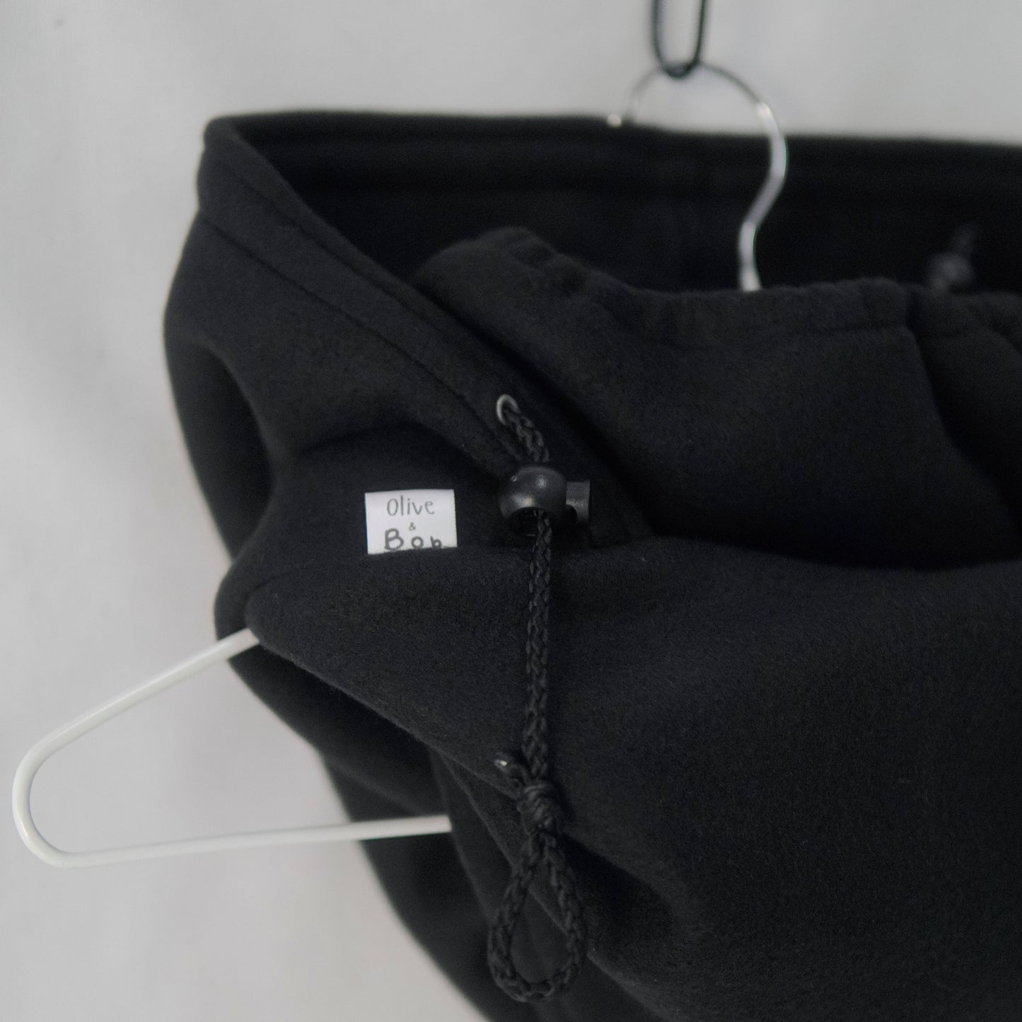 A handmade Noir Hoodeanie in solid black, displayed to show its soft, cozy fabric and new adjustable face panel feature. The design allows the hood to be pulled up snugly over the nose for added warmth and comfort, blending functionality with minimalist streetwear style.