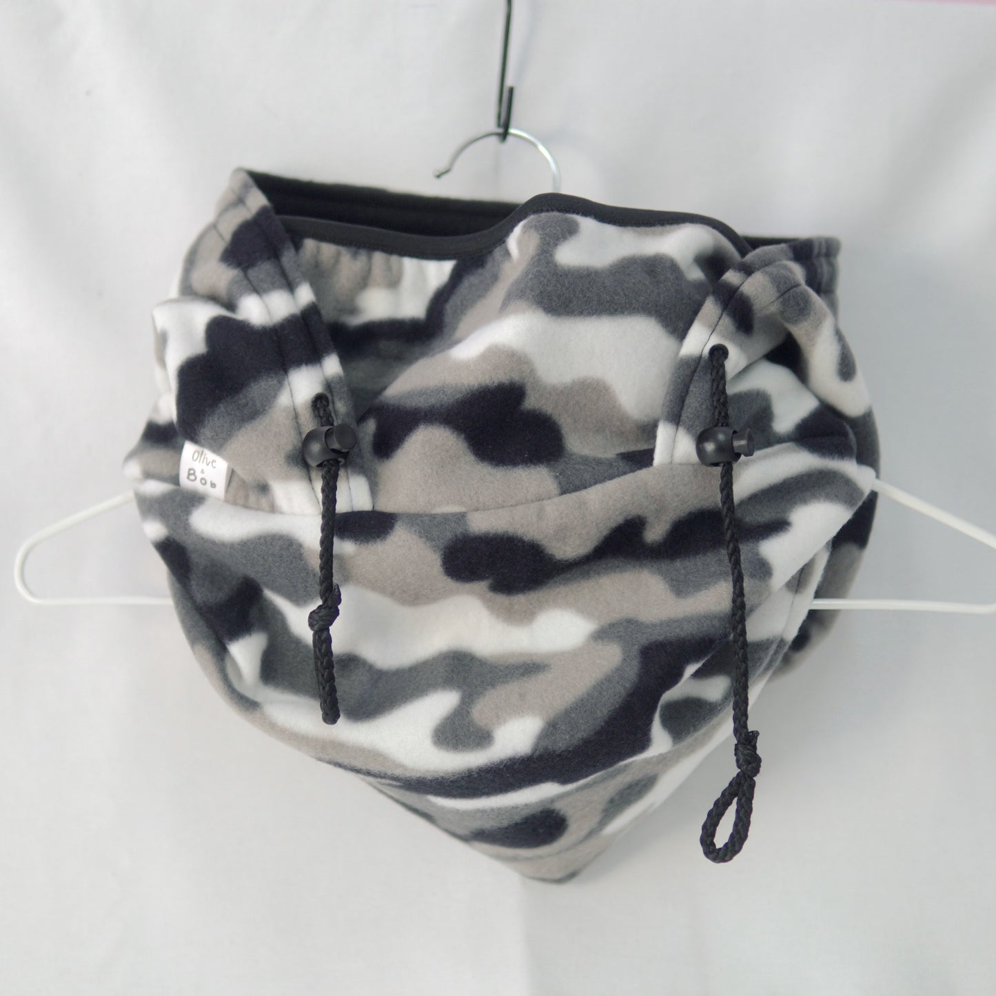 A handmade Tundra Camo Hoodeanie displayed on a flat surface, featuring a soft, cozy fabric in a grey and black camouflage print. The garment combines the relaxed fit of a hoodie with the snug warmth of a beanie, designed for comfort, movement, and style.