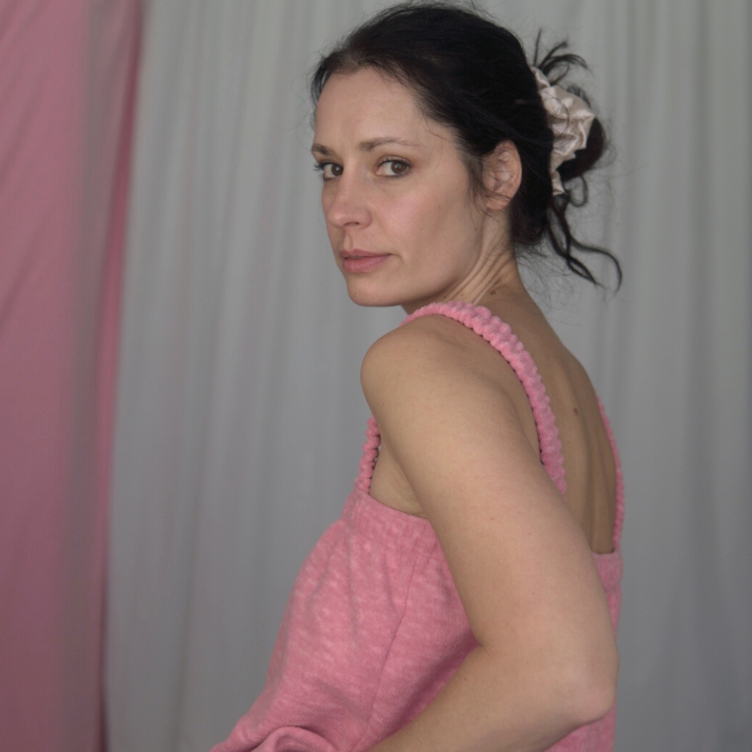 A pink fleece jumpsuit on a model with a soft fabric backdrop. The jumpsuit features elasticated straps, an elastic underarm band, and gathered elastic cuffs at the ankles.