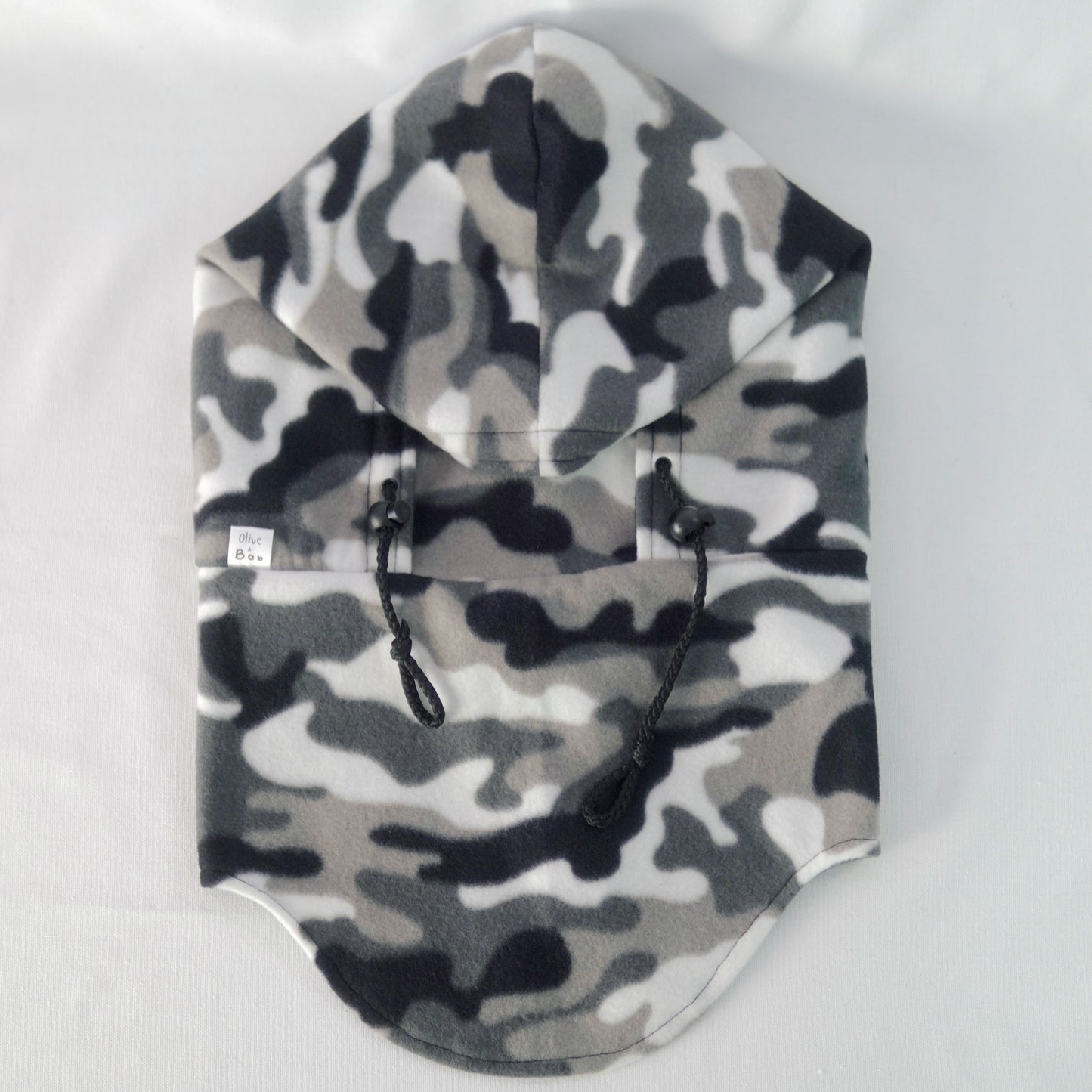 A handmade Tundra Camo Hoodeanie displayed on a flat surface, featuring a soft, cozy fabric in a grey and black camouflage print. The garment combines the relaxed fit of a hoodie with the snug warmth of a beanie, designed for comfort, movement, and style.