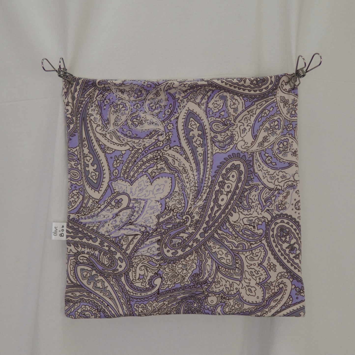 This is a flat-lay image of a tube top featuring an intricate paisley pattern in shades of lavender, cream, and gray. The fabric is displayed neatly with clips at the corners, showcasing the detailed design and vibrant color contrast. A small branded fabric label is visible on the left seam, adding a refined touch.