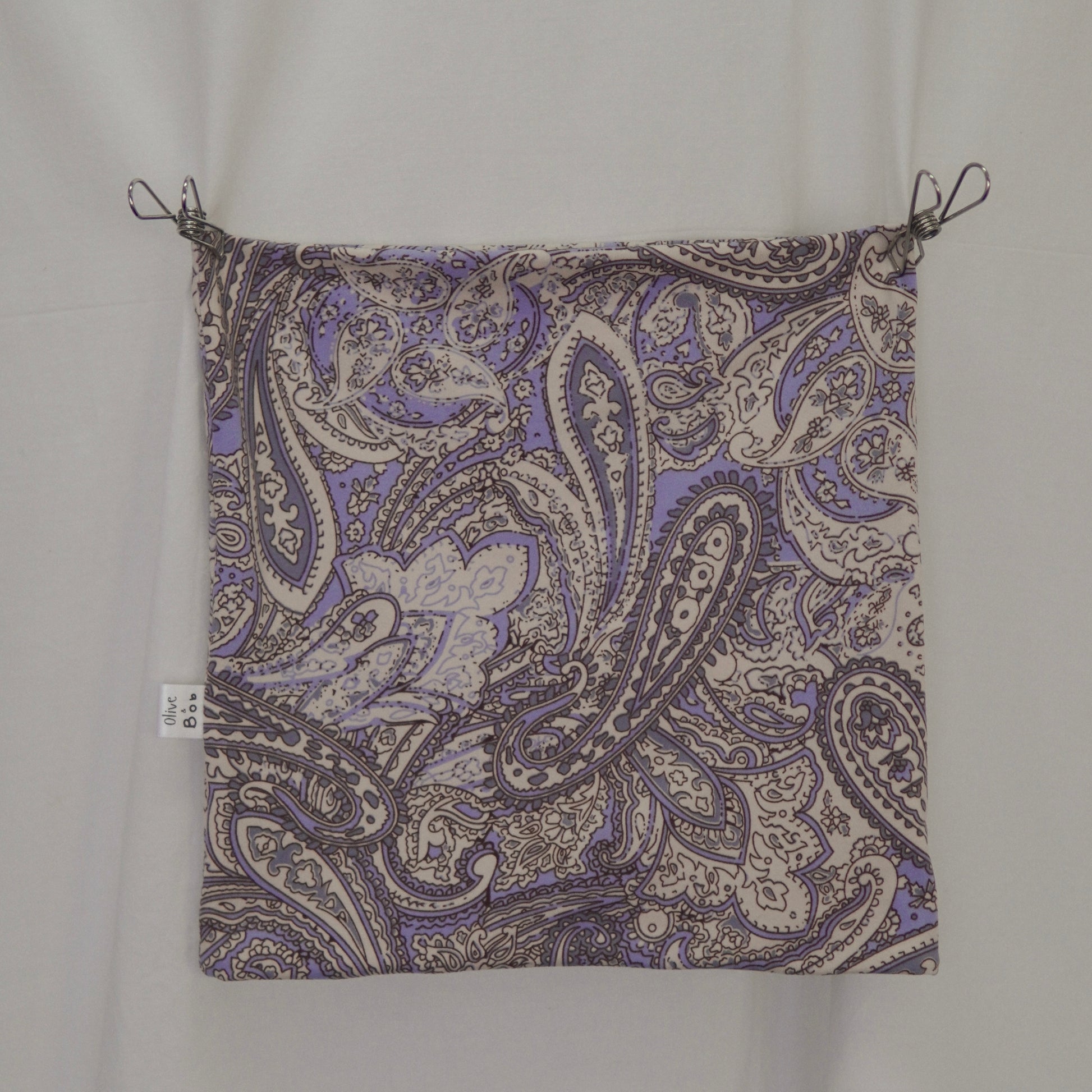 This is a flat-lay image of a tube top featuring an intricate paisley pattern in shades of lavender, cream, and gray. The fabric is displayed neatly with clips at the corners, showcasing the detailed design and vibrant color contrast. A small branded fabric label is visible on the left seam, adding a refined touch.